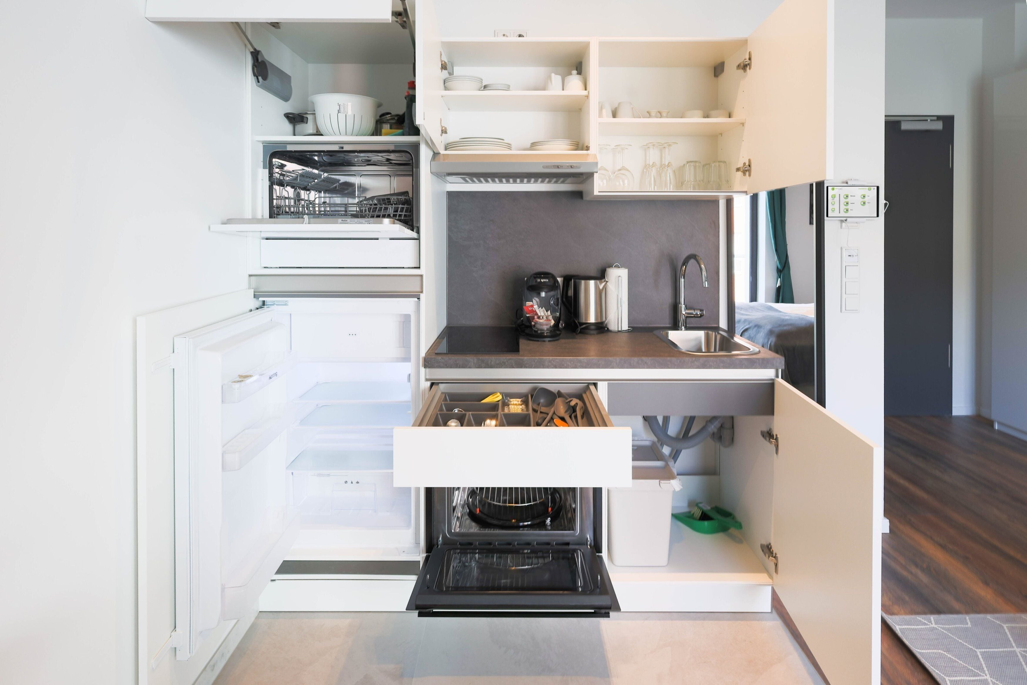 Uma cozinha compacta com eletrodomésticos embutidos, incluindo lava-louças, forno e máquina de café.