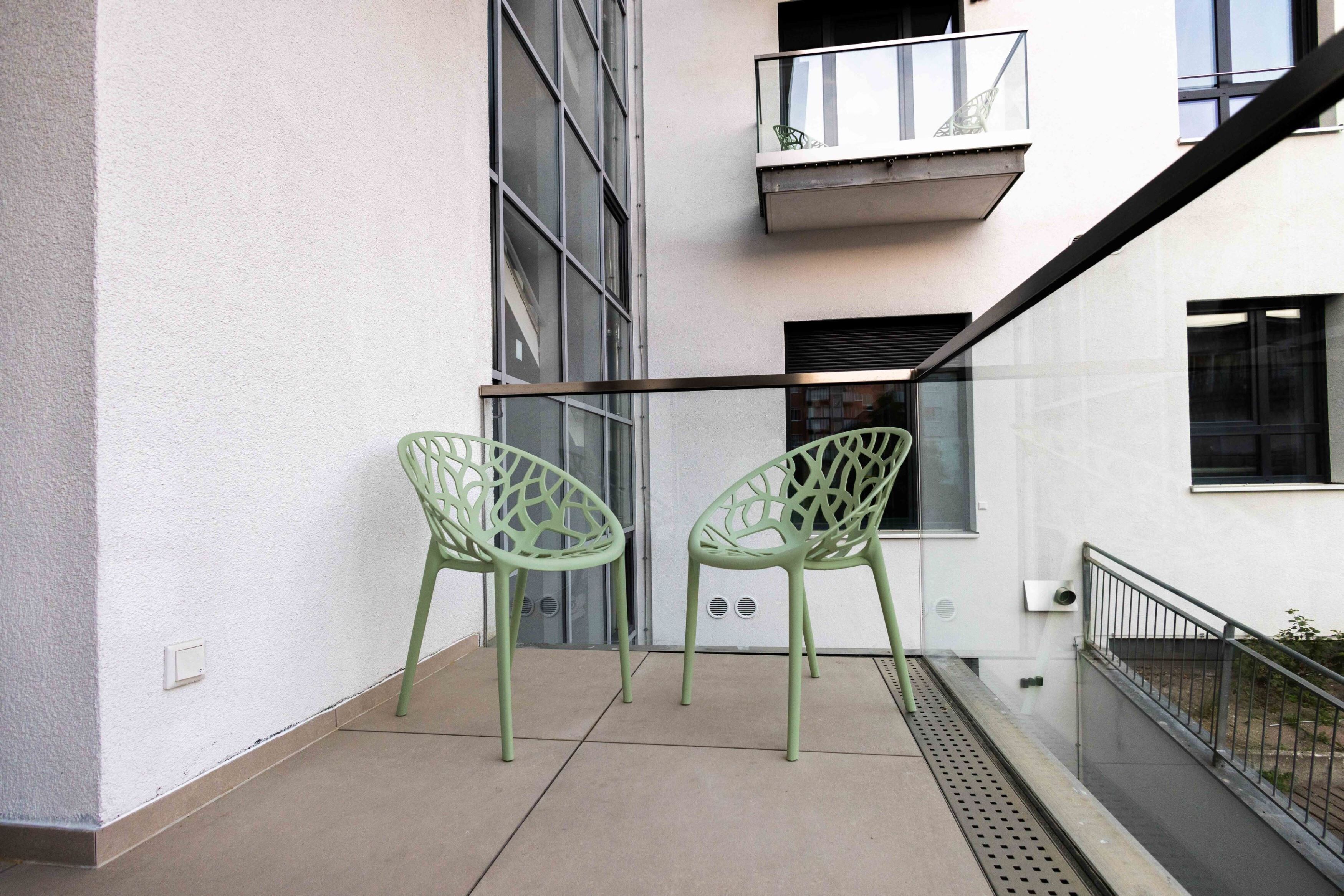 Un balcon avec deux chaises vertes et une rambarde en verre.