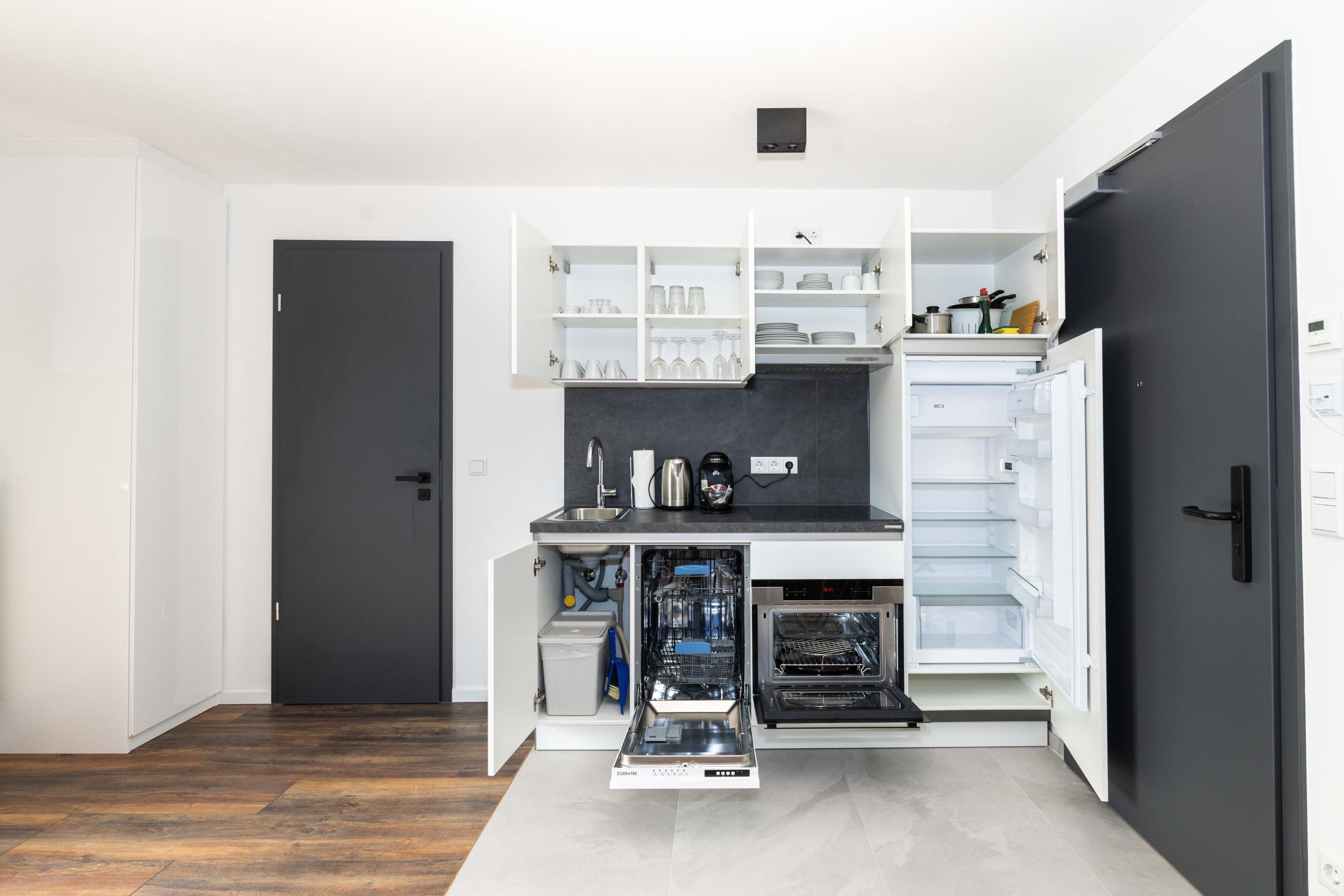 A compact kitchen with integrated appliances, including a dishwasher and oven, and a built-in wine rack.