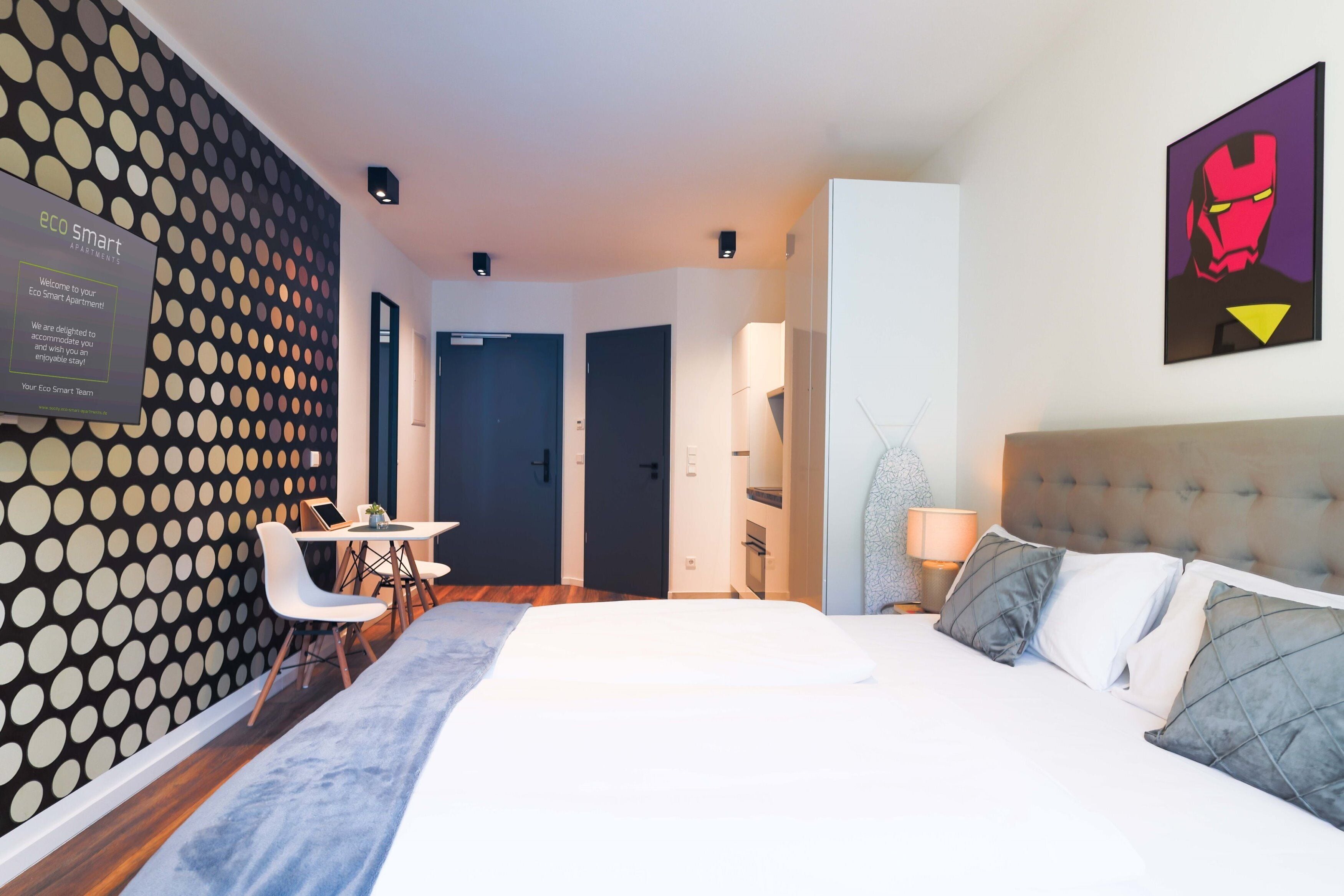 Ein modernes Hotelzimmer mit Bett, Schreibtisch und an der Wand montiertem Bildschirm, der die Marke „eco smart“ zeigt.