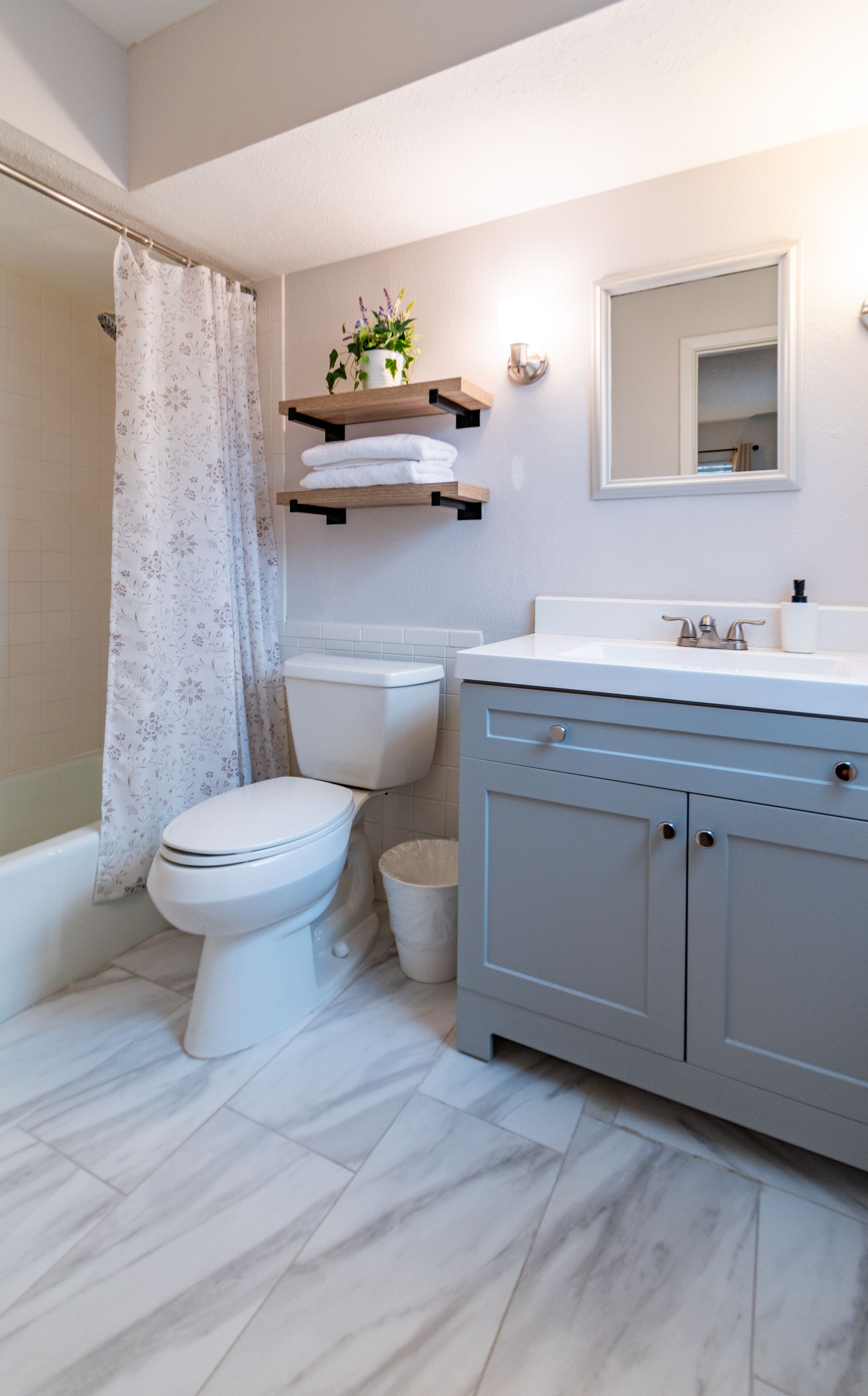 Ein Badezimmer mit Toilette, Dusche, Waschtisch mit Spiegel und einem Blumentopf auf einem Regal.