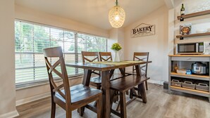 A dining area with a wooden table and chairs, a hanging light fixture, a window with blinds, and a kitchen area with a microwave and shelves. - Brandon Peaceful Home w/newly renovated kitchen (Brandon)