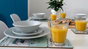 A breakfast setup with bowls, plates, and glasses of orange juice on a table with newspapers underneath. - Judah Suite by Koya Homes (Barry)