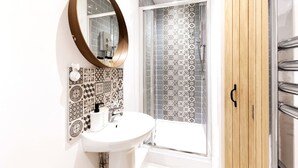 A bathroom with a white sink, a round mirror, patterned tiles, and a shower enclosure.