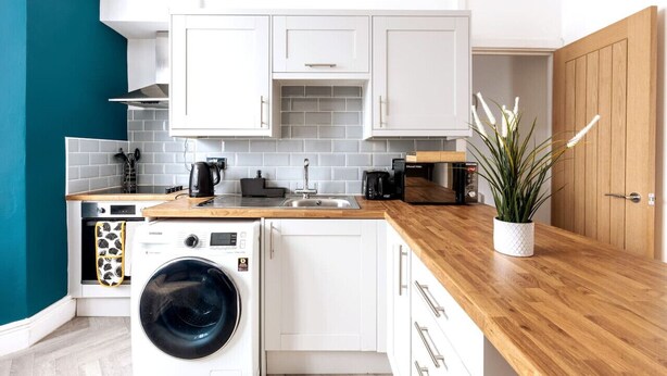 A compact kitchen with white cabinets, a wooden countertop, a washing machine, and a microwave.