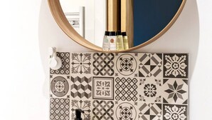 A bathroom with a round mirror, a gold faucet, and patterned tiles.