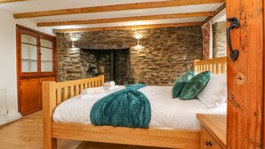 Ein hölzernes Bett mit weißer Bettwäsche und türkisfarbenen Kissen in einem Zimmer mit freiliegenden Holzbalken und Steinwänden.