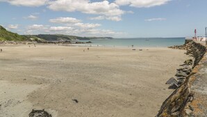 Ein weiter Sandstrand mit einem steinernen Wellenbrecher rechts, blauem Himmel und ruhiger See.
