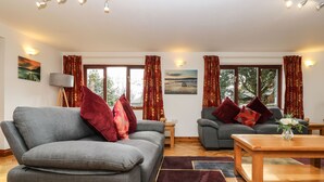 Ein modernes Wohnzimmer mit zwei grauen Sofas, roten und orangen Kissen, einem Holztisch und einem großen Fenster mit Vorhängen.