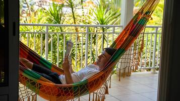 Una persona recostada en una hamaca en un balcón, con vista a plantas tropicales.