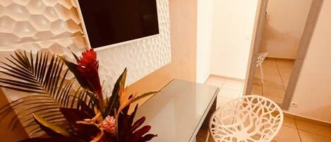 A modern room with a flat-screen TV mounted on a textured wall, a white cabinet, a white chair, and a large mirror.