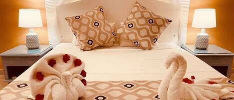 Un lit à baldaquin, deux lampes de chevet, des coussins à motifs et une couverture parsemée de pétales de rose.