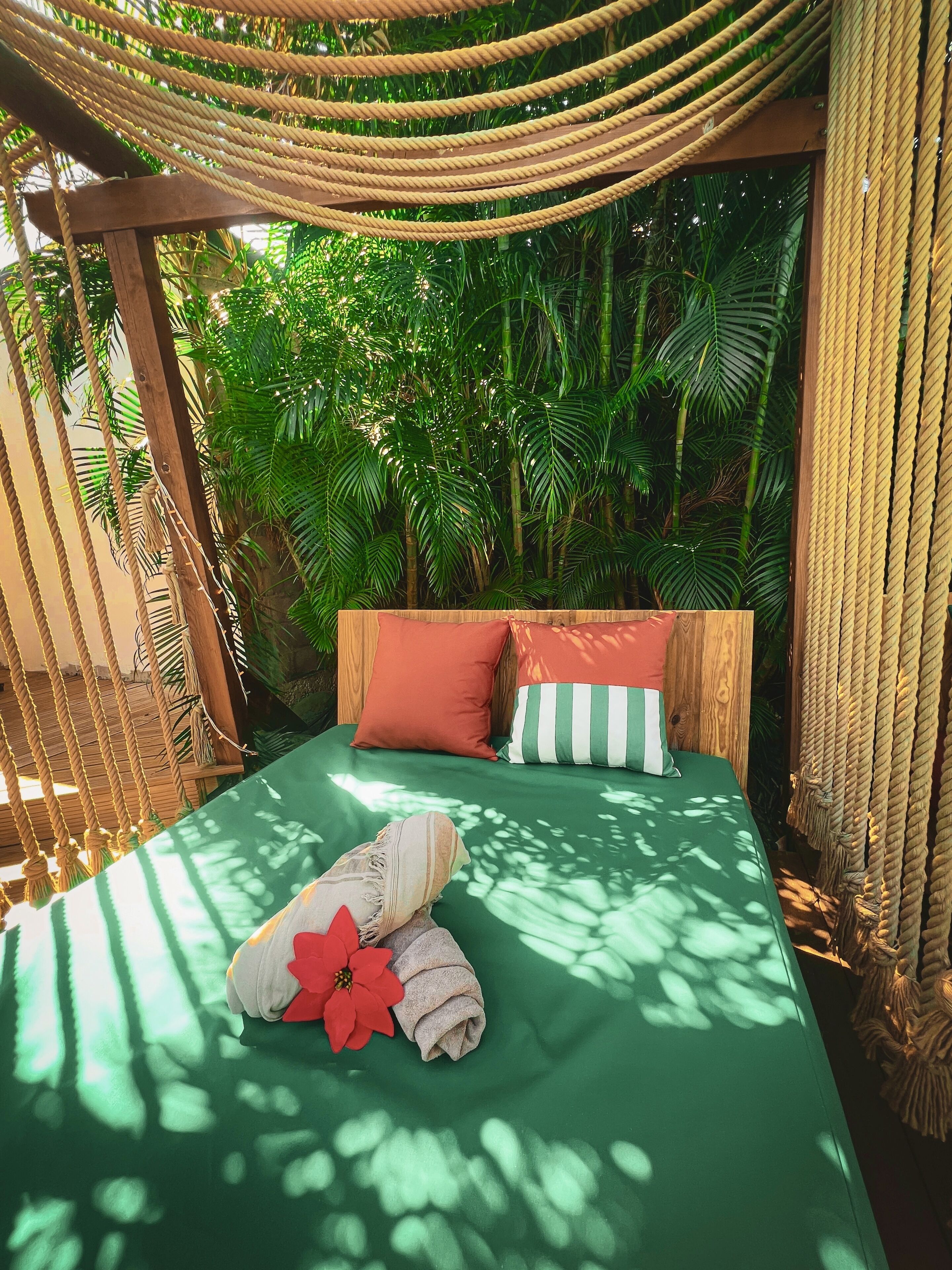 Una hamaca con un edredón verde, dos almohadas y una decoración floral roja.