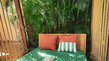 Una hamaca con un edredón verde, dos almohadas y una decoración floral roja.