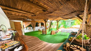 A buffet setup with various food items, a wooden floor, and a thatched roof structure. - Tropicana Suites (Deshaies)