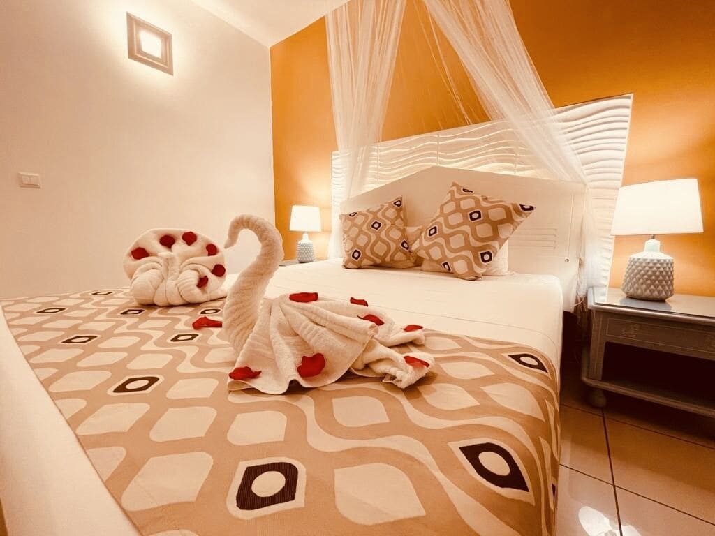 Una habitación de hotel con cama, una mesita de noche con lámpara y un cojín decorativo con forma de cisne.