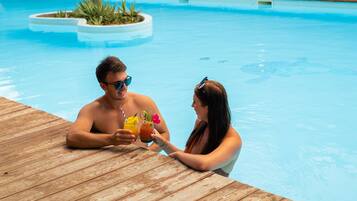 A poolside area with a wooden deck, a palm tree, and lush greenery in the background.