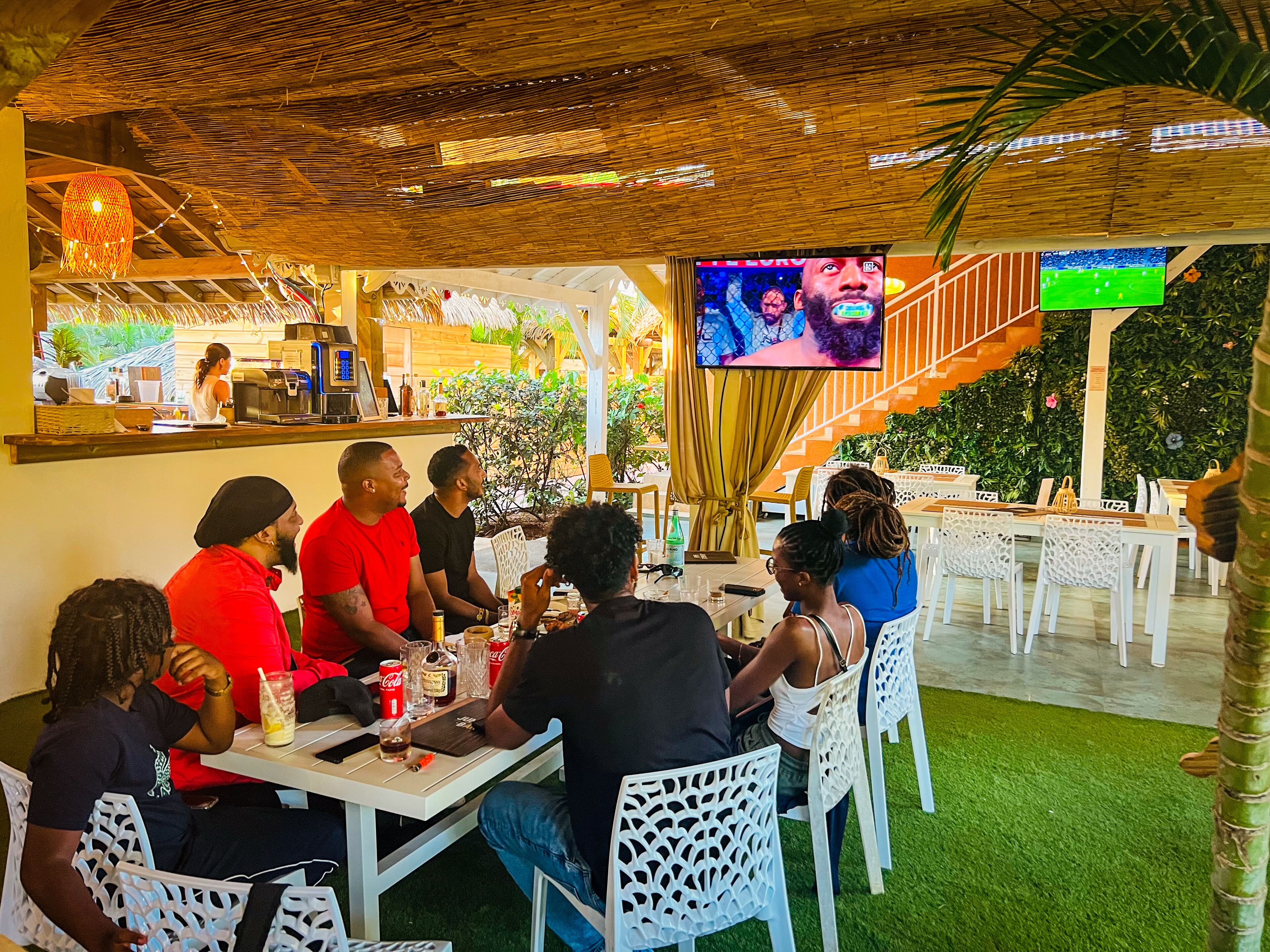 Un restaurant amb terrassa, zona de bar i una pantalla que mostra un programa.