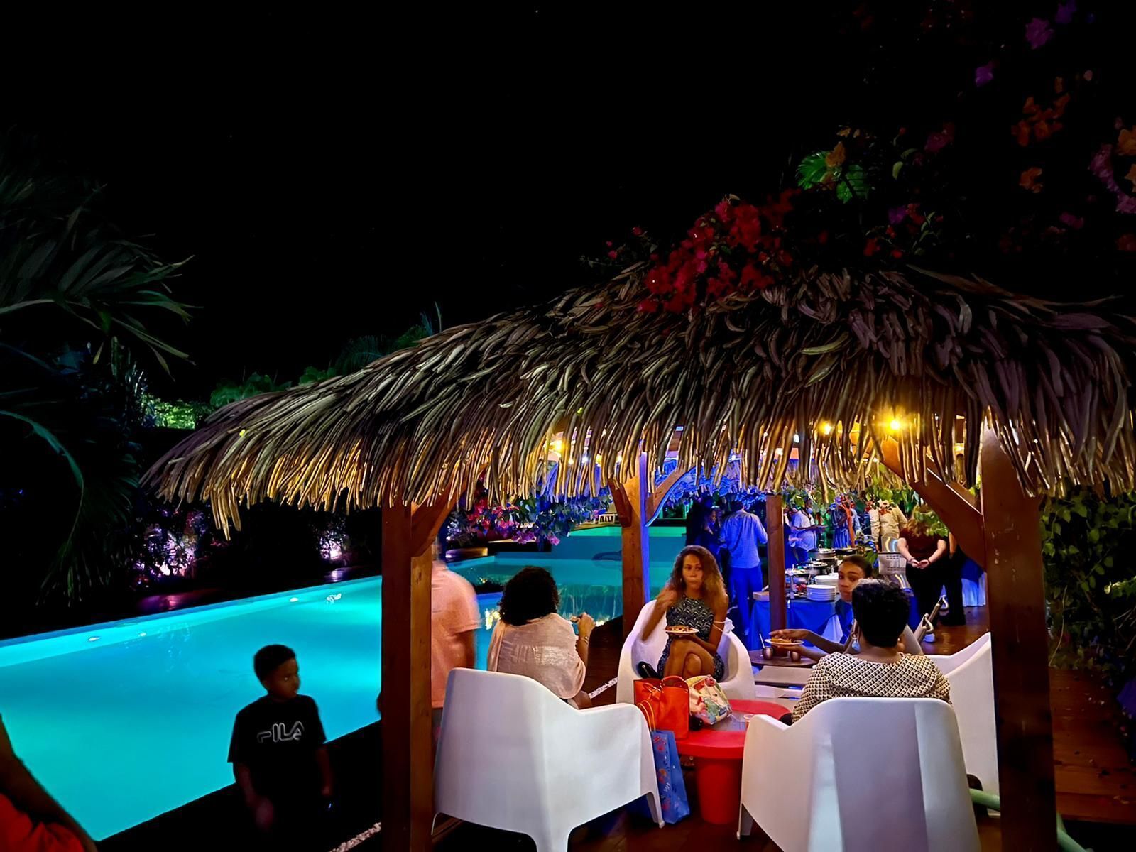 Un espace aménagé au bord de la piscine, doté d’une structure avec toit de chaume, de tables et de chaises.