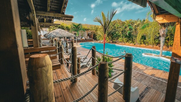 A wooden deck with a rope barrier, a pool, and lounge chairs. - Tropicana Suites (Deshaies)