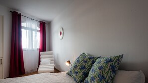 A bedroom with a bed, pillows, a nightstand, a wall clock, and a window with curtains.