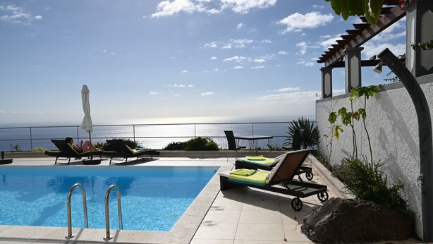 A pool area with lounge chairs and an umbrella, overlooking a body of water.