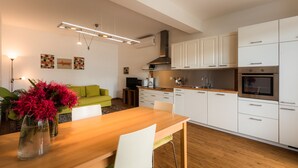 A modern kitchen with white cabinets, a wooden dining table, and a green sofa in the living area.