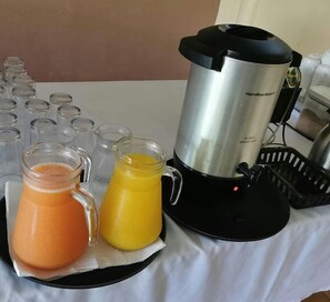 A kitchen area with a Hamilton Beach blender, two pitchers of juice, and several empty glasses.