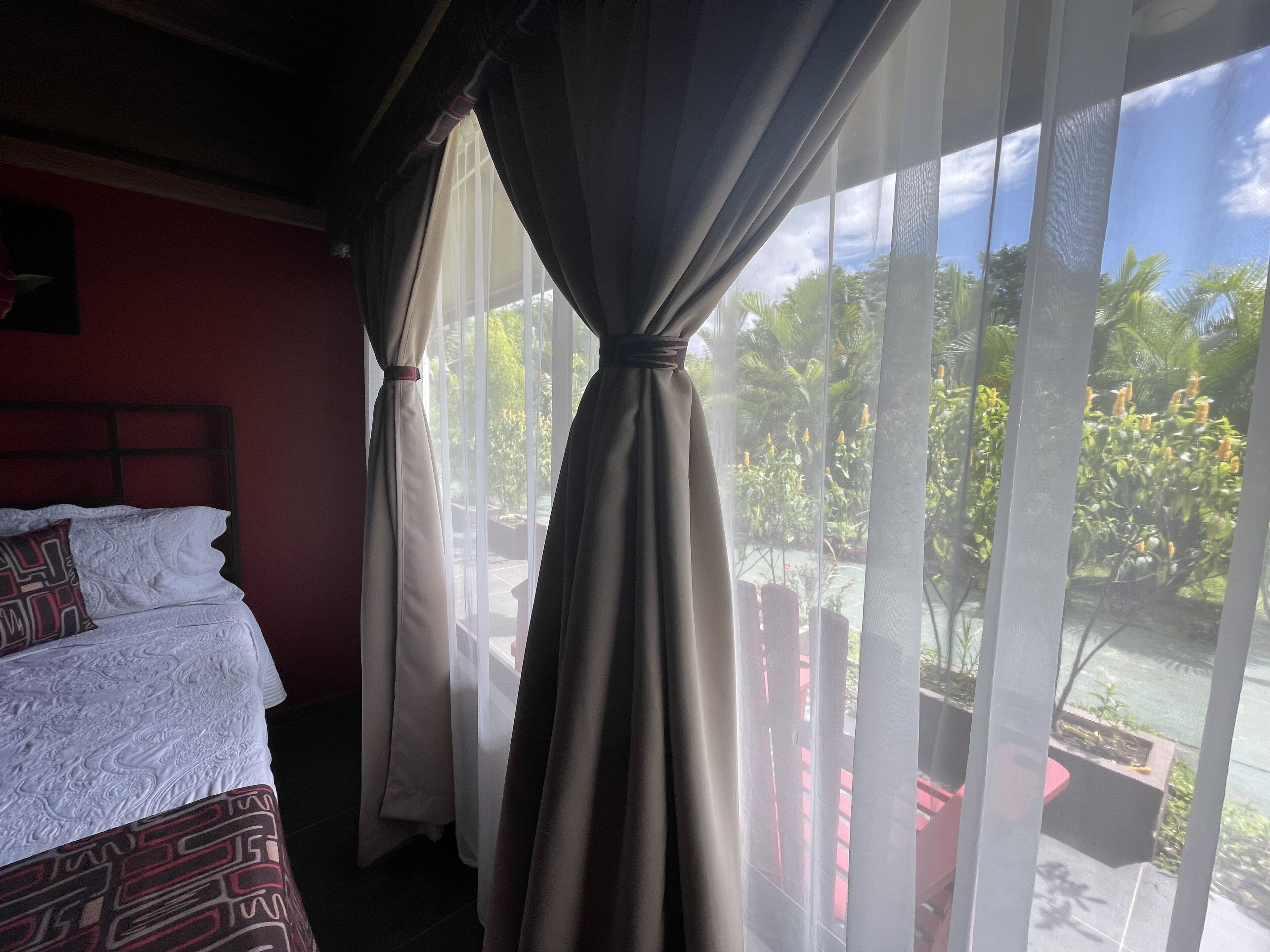 A hotel room with a bed, curtains, and a view of the outdoors.