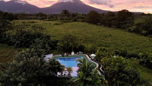 Un resort con piscina rodeado de exuberante vegetación y una montaña al fondo.