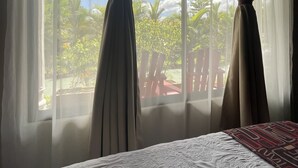 Una cama con una colcha estampada, cortinas translúcidas y vistas a muebles de exterior y follaje.