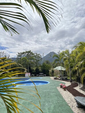 A pool area with two circular pools, surrounded by palm trees and greenery, with a mountain in the background.