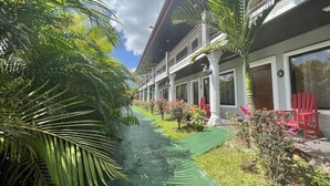 Un hotel con un corredor cubierto, palmeras y sillas rojas.