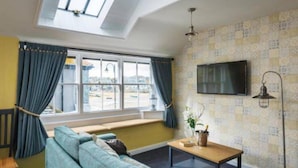 A room with a sofa, a table, a TV, and a window with curtains. - Lifeboat Inn (St Ives)