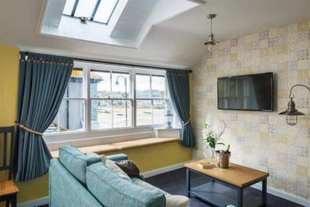 A room with a sofa, a table, a TV, and a window with curtains.