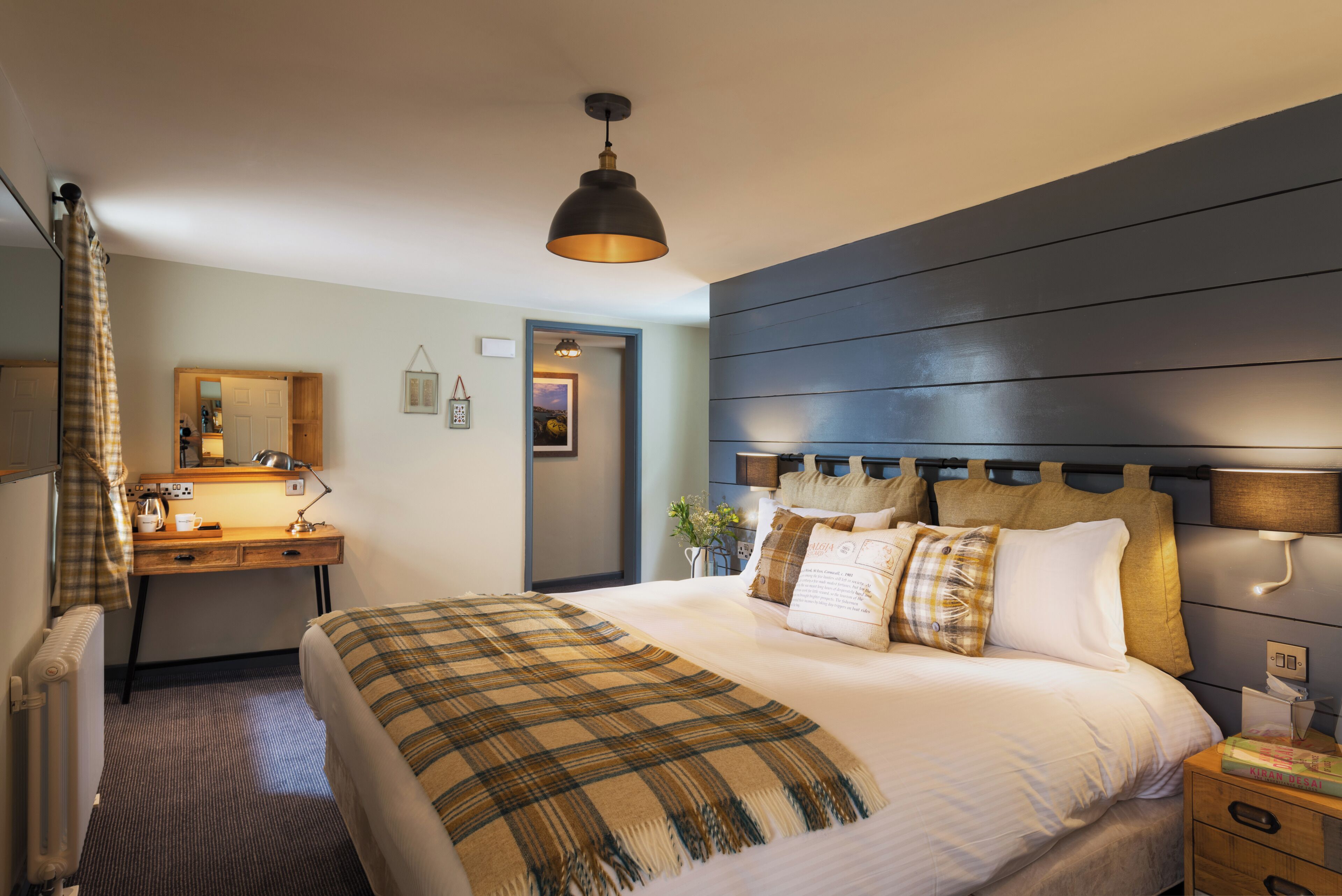 A hotel room with a bed, a desk, a chair, a mirror, a radiator, and a window.