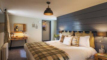 A hotel room with a bed, a desk, a chair, a mirror, a radiator, and a window.