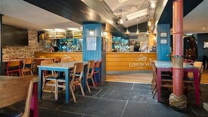 A restaurant with a bar area, wooden tables and chairs, and a stone wall. - Lifeboat Inn (St Ives)
