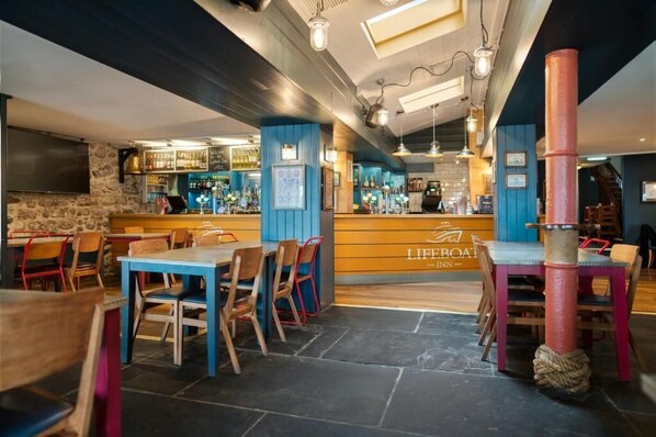 A restaurant with a bar area, wooden tables and chairs, and a stone wall. - Lifeboat Inn (St Ives)