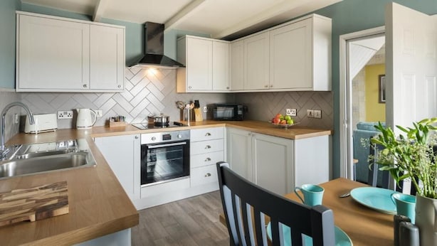 A modern kitchen with white cabinets, a microwave, a stove, and a sink. - Lifeboat Inn (St Ives)