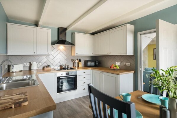 A modern kitchen with white cabinets, a microwave, a stove, and a sink. - Lifeboat Inn (St Ives)