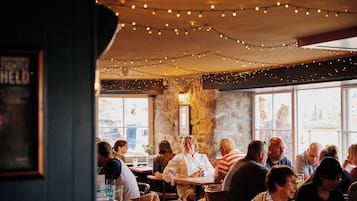 Interior de restaurante con paredes de piedra, luces colgantes y clientes sentados en mesas.