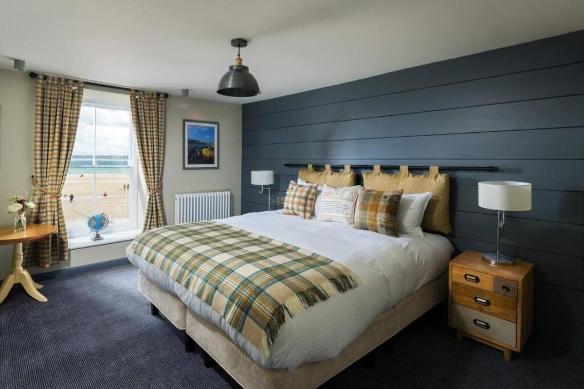 A bedroom with a bed, bedside tables, a window with curtains, a lamp, and a view of the beach.