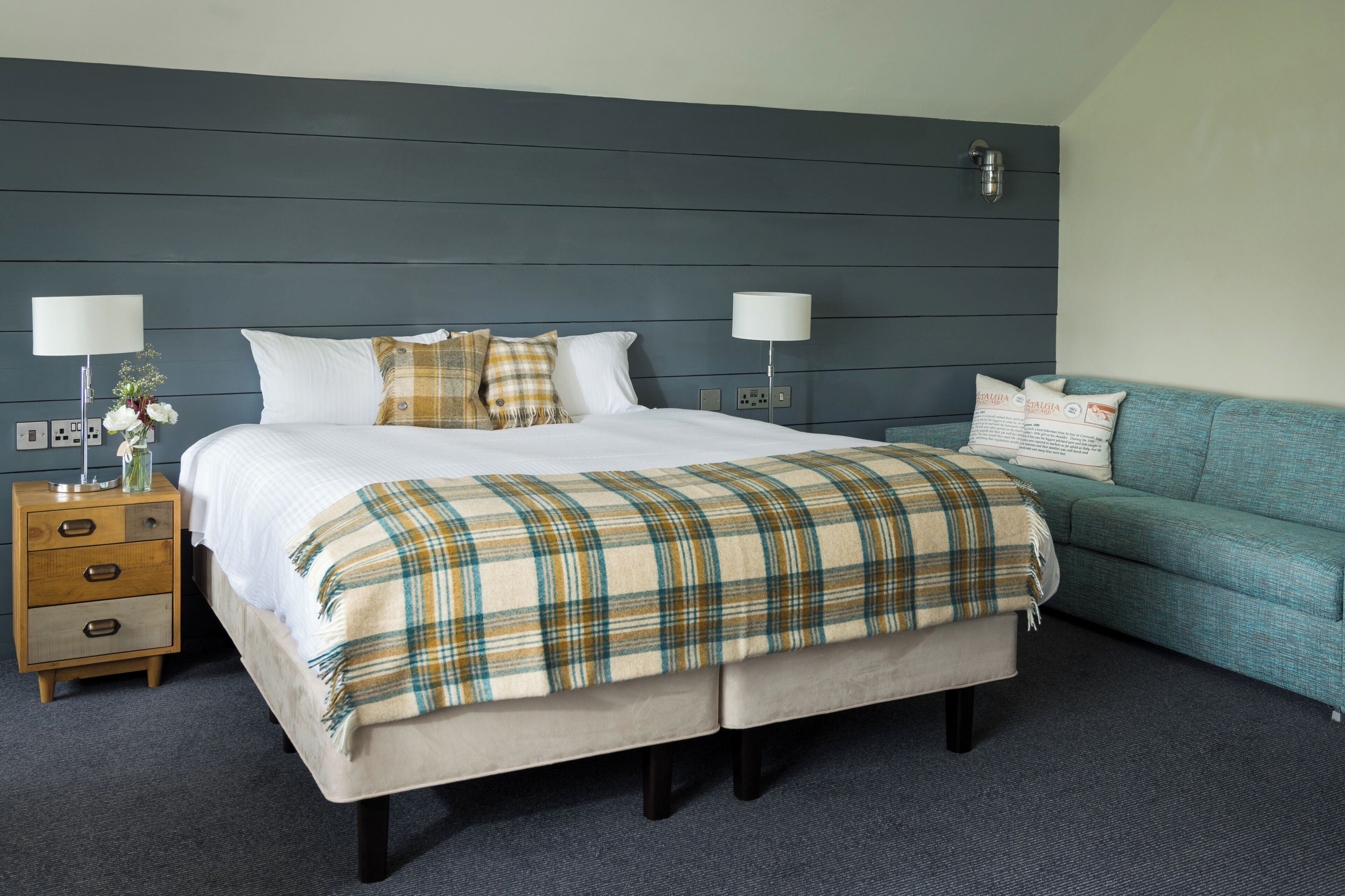 A hotel room with a bed, bedside tables, a lamp, a sofa, and a carpeted floor.
