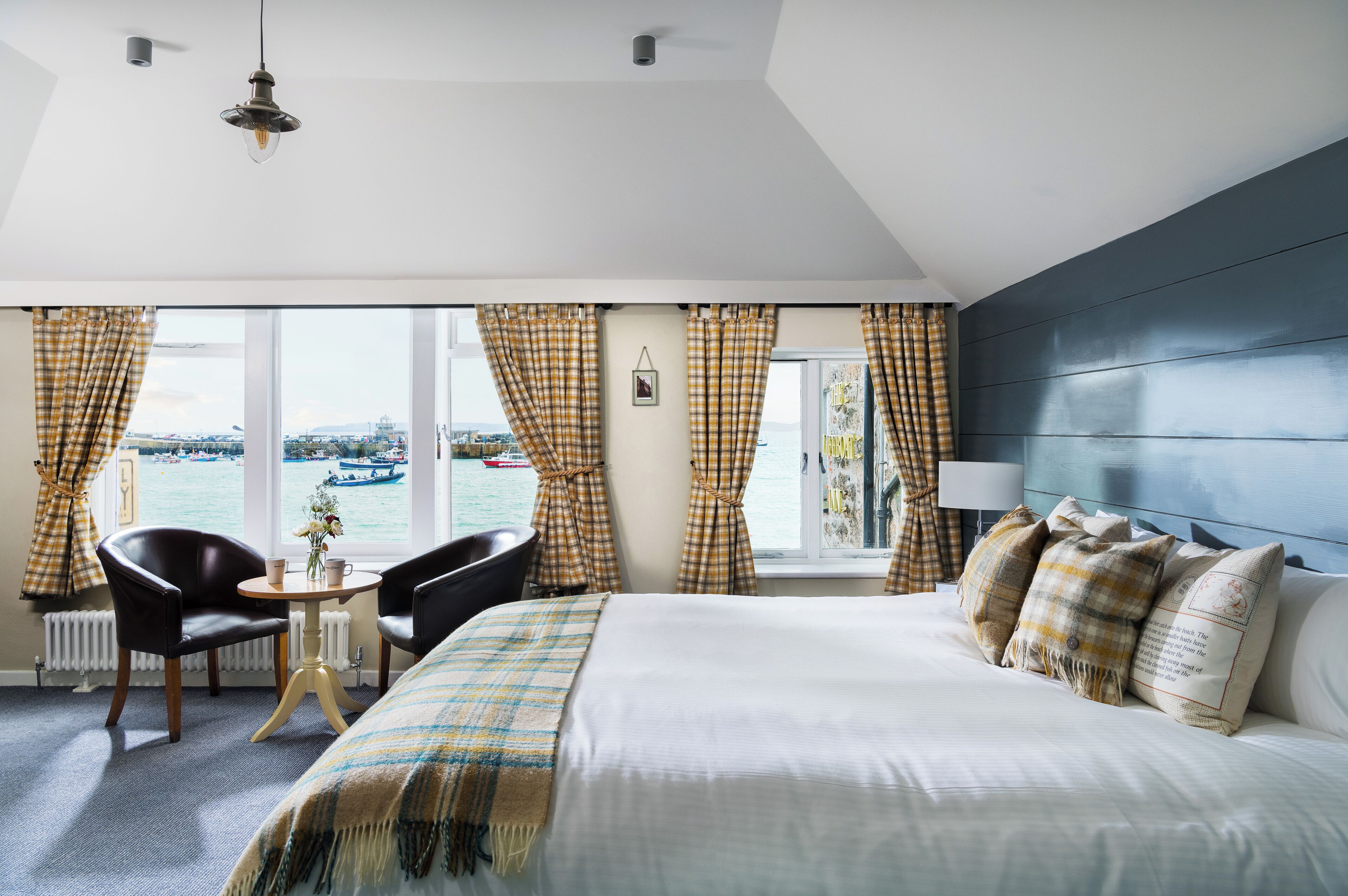 A hotel room with a bed, a table with chairs, a view of the sea, and a window with curtains.