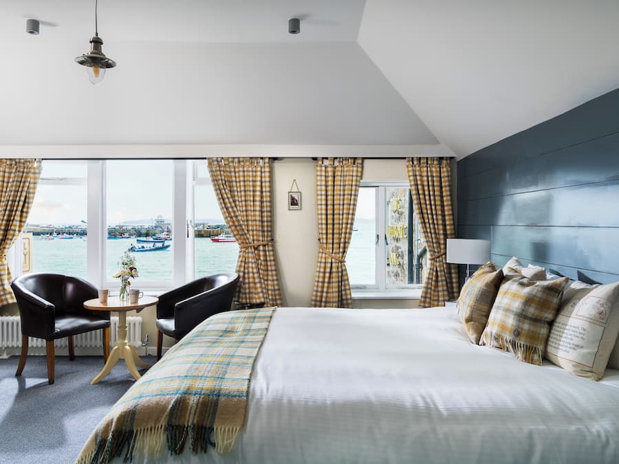 Una camera d'albergo con un letto, un tavolo con sedie, vista mare e una finestra con tende.