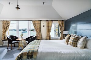A hotel room with a bed, a table with chairs, a view of the sea, and a window with curtains. - Lifeboat Inn (St Ives)