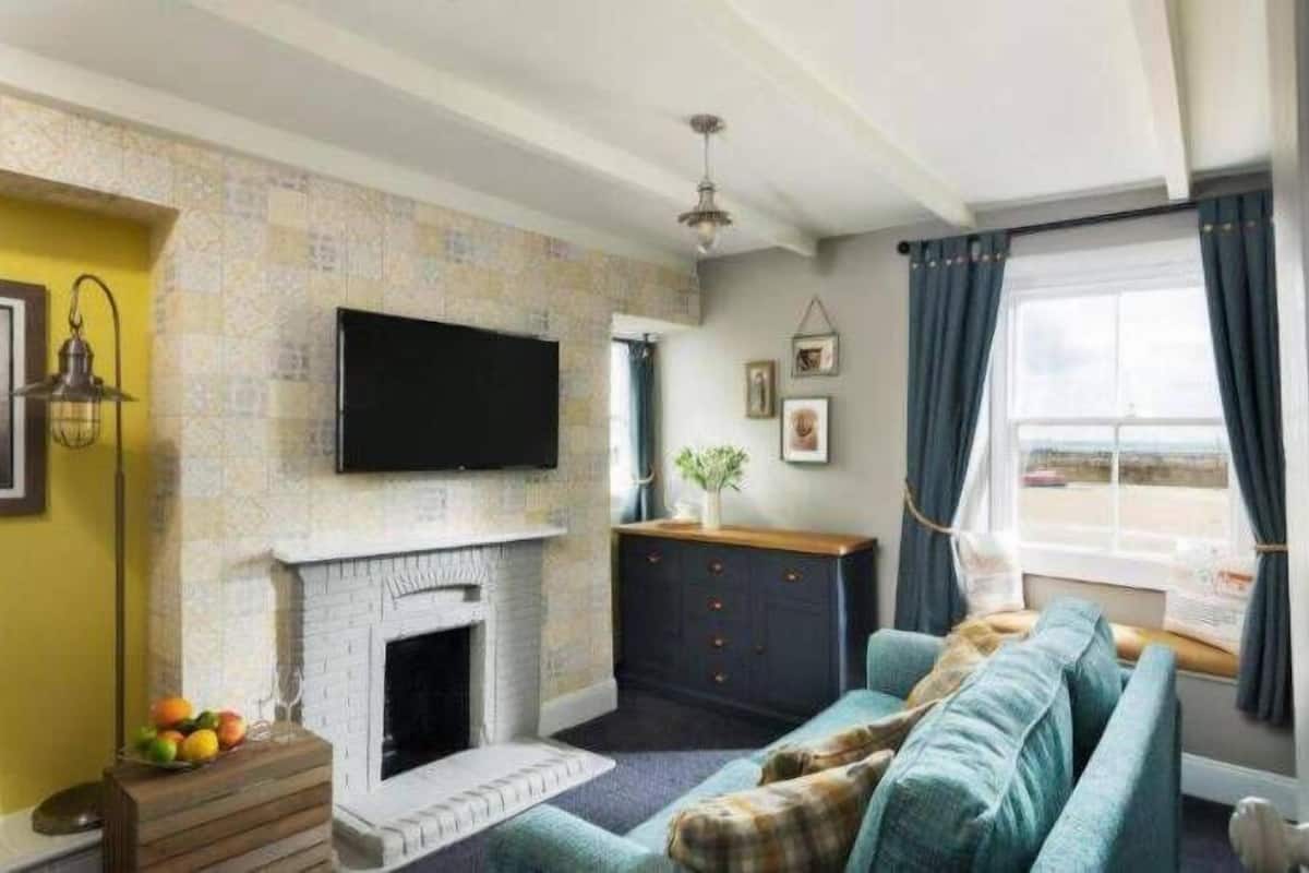 A living room with a fireplace, a sofa, a television, and a window with curtains.