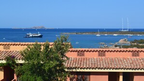 A coastal view with a building featuring a tiled roof and a view of the sea with boats and a distant island. - Casa Azul, Seaview terrace, private parking, pool (Golfo Aranci)