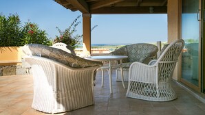 A covered outdoor seating area with wicker furniture, a table, and a view of the ocean. - Casa Azul, Seaview terrace, private parking, pool (Golfo Aranci)